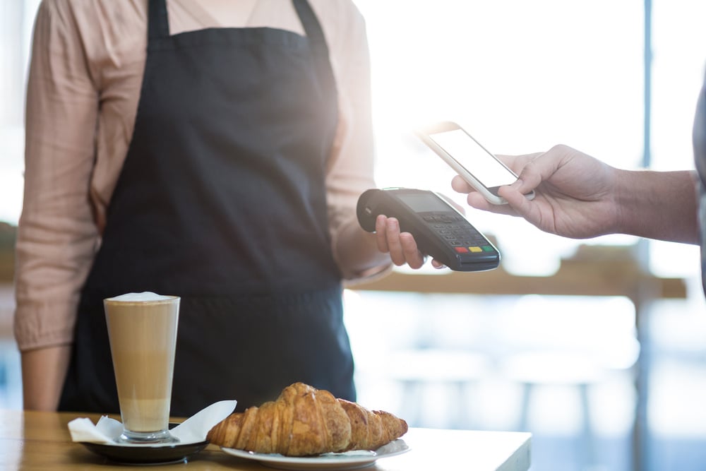 Man paying bill through smartphone using NFC technology in cafe-1 Man paying bill through smartphone using NFC technology in cafe-1